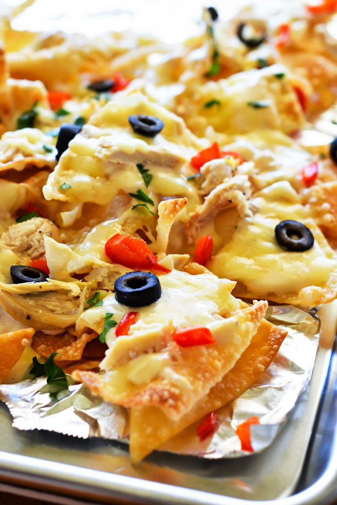 These Italian nachos are made with crispy wontons, grilled chicken, bell peppers, and olives smothered in&nbsp;Alfredo sauce and cheese. Life-in-the-Lofthouse.com