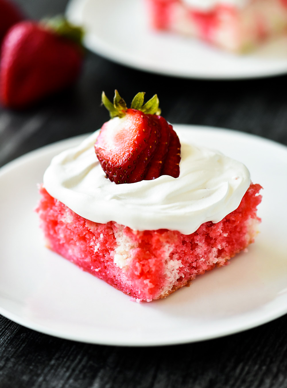 Incredibly light and delicious Strawberry Jello Poke Cake! This white cake is filled with strawberry jello and topped with fresh whipped cream and strawberries.