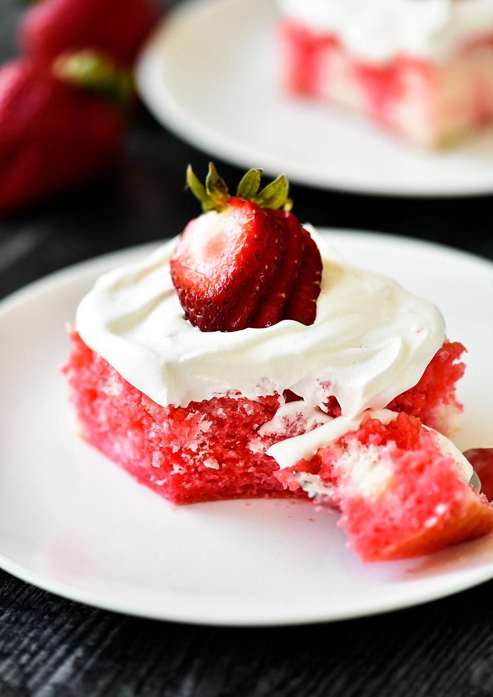 Incredibly light and delicious Strawberry Jello Poke Cake! This white cake is filled with strawberry jello and topped with fresh whipped cream and strawberries.