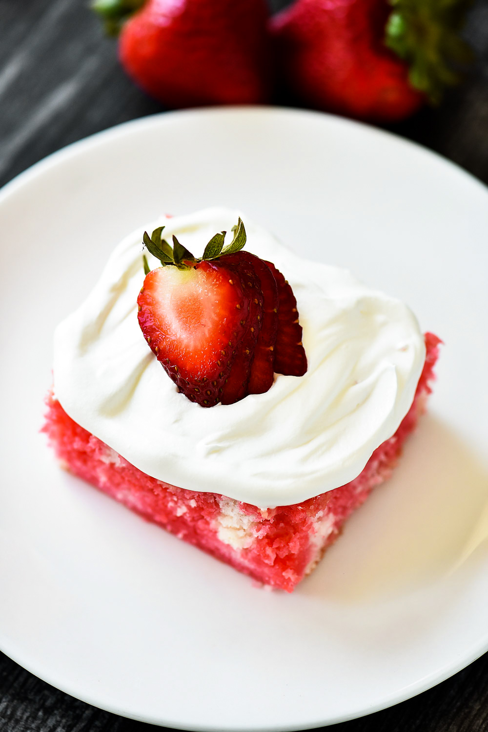 Incredibly light and delicious Strawberry Jello Poke Cake! This white cake is filled with strawberry jello and topped with fresh whipped cream and strawberries.
