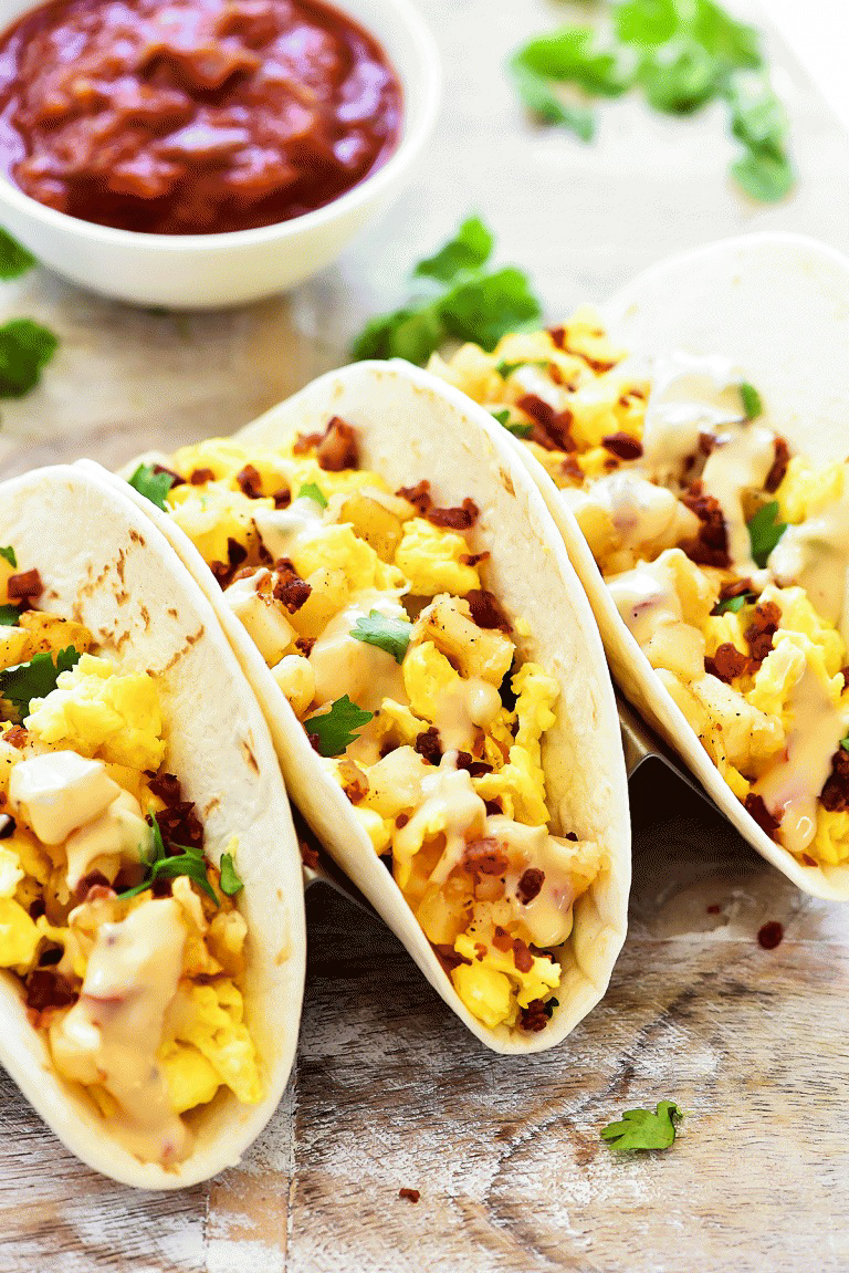 Breakfast Tacos filled with scrambled eggs, crispy bacon, seasoned potatoes and drenched in Queso cheese sauce. Life-in-the-Lofthouse.com
