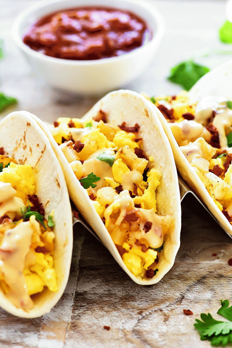 Breakfast Tacos filled with scrambled eggs, crispy bacon, seasoned potatoes and drenched in Queso cheese sauce. Life-in-the-Lofthouse.com