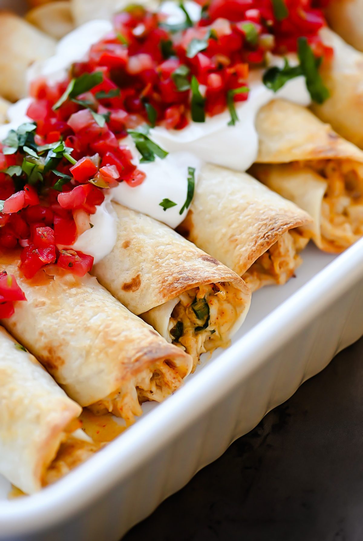 Baked Chicken Taquitos are a crispy flour tortilla wrapped around a warm center of creamy and cheesy Mexican chicken.