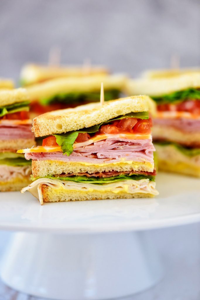 Club Sandwiches are stacked with ham, turkey, cheese, lettuce and tomato with a mustard and mayo mixture.