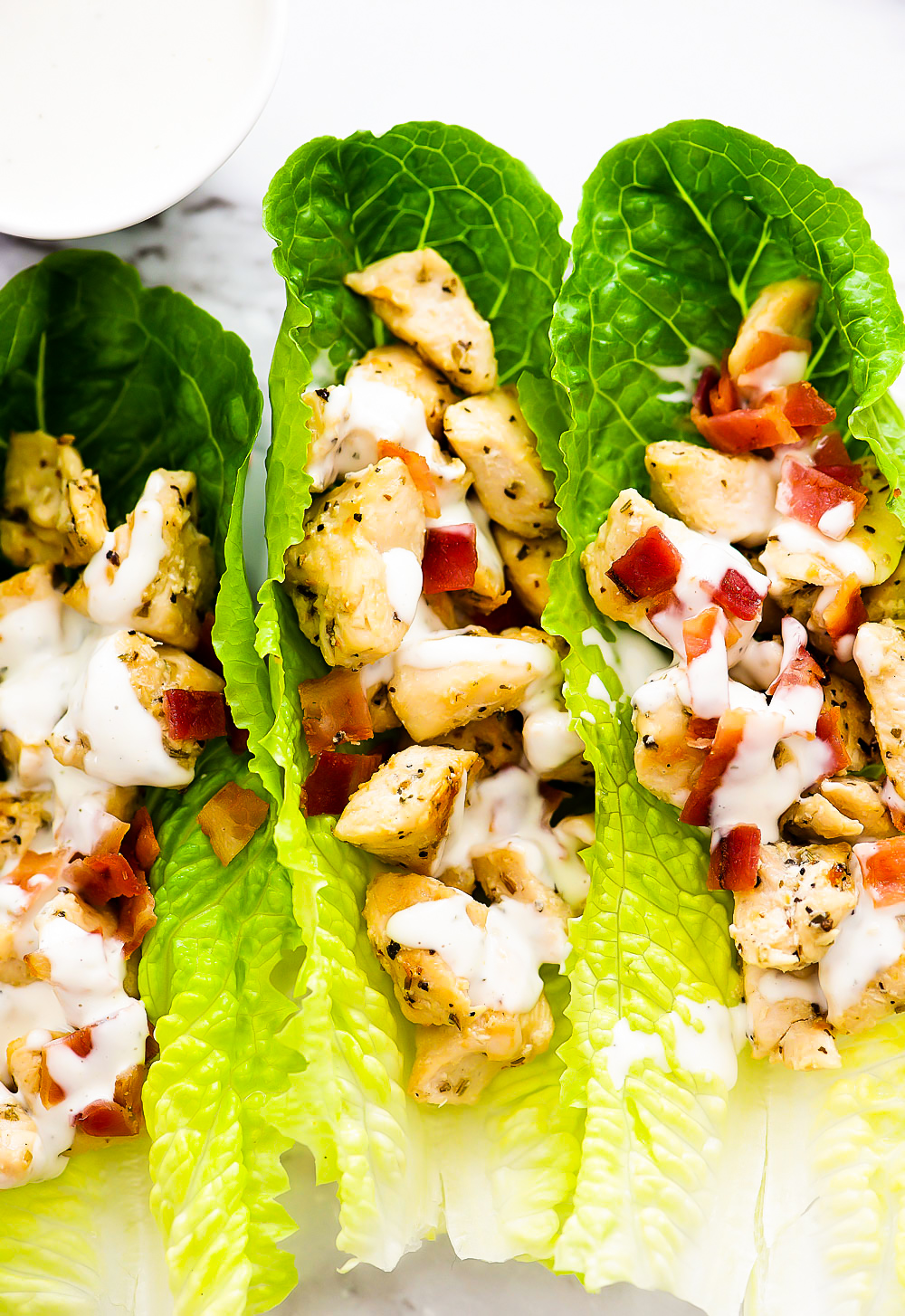 Seasoned chicken and crumbled bacon are filled inside of romaine lettuce leaves. They are topped off with ranch dressing.