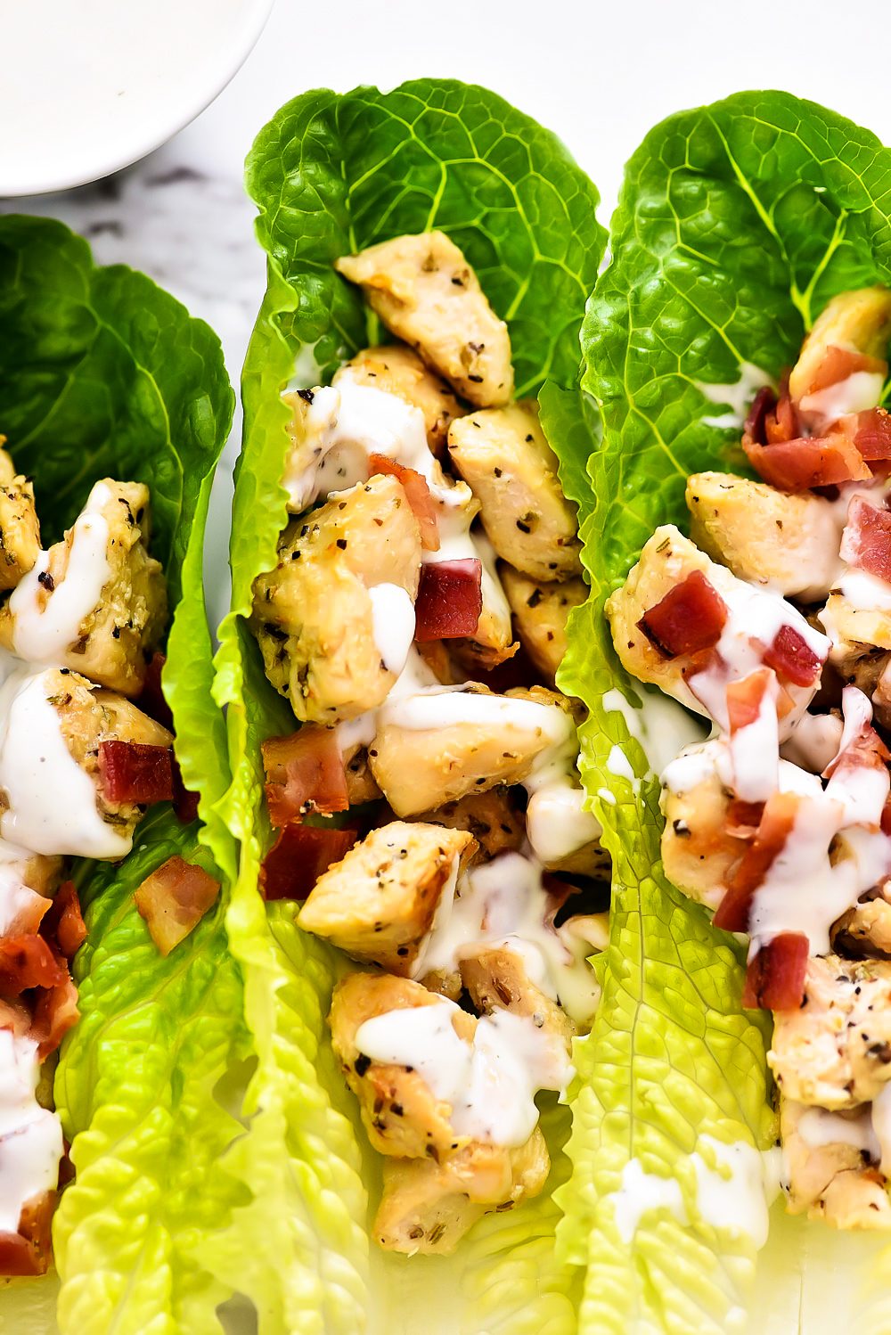 Seasoned chicken and crumbled bacon are filled inside of romaine lettuce leaves. They are topped off with ranch dressing.