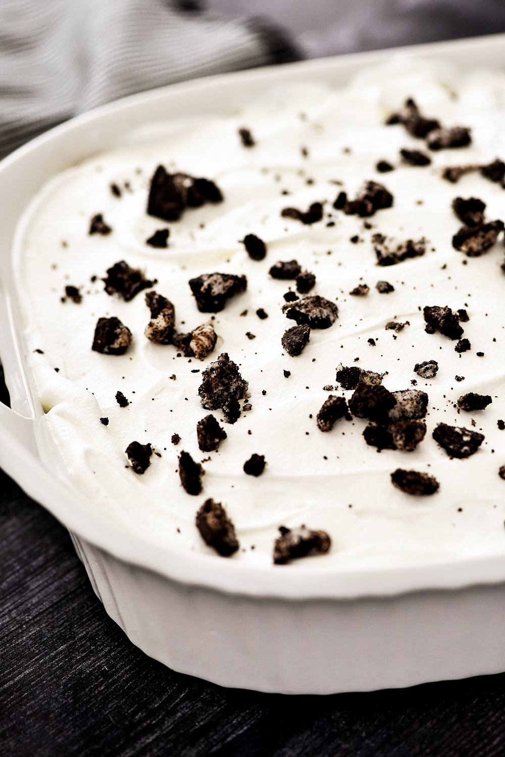 Oreo Pudding Poke Cake starts with a chocolate cake, then holes are poked in the cake and Oreo Pudding is poured inside the holes. The cake is topped off with cool whip and crushed Oreo cookies.