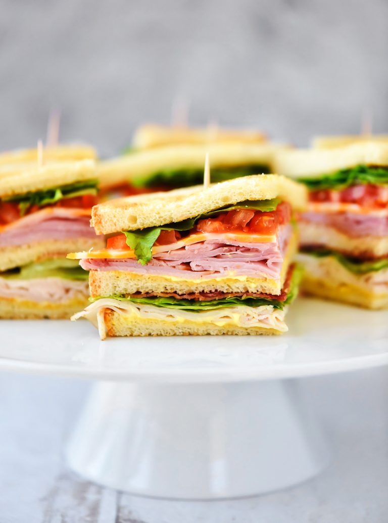 Club Sandwiches are stacked with ham, turkey, cheese, lettuce and tomato with a mustard and mayo mixture.